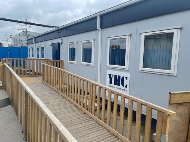 Large modular building installed onsite with wooden decking and ramp leading to the entrance.